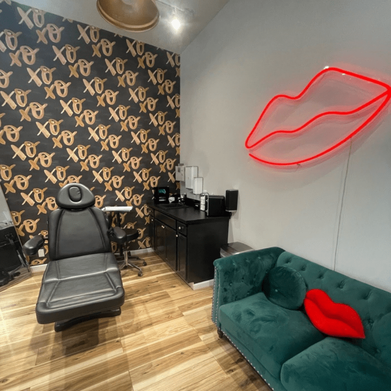 Treatment room with green velvet couch and black blush chair with neon lips on the wall