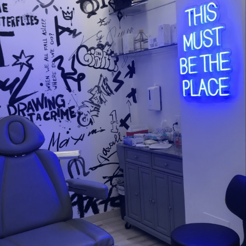 Treatment room in Evolve Med Spa with black plush chair and neon sign on wall that reads "this must be the place"