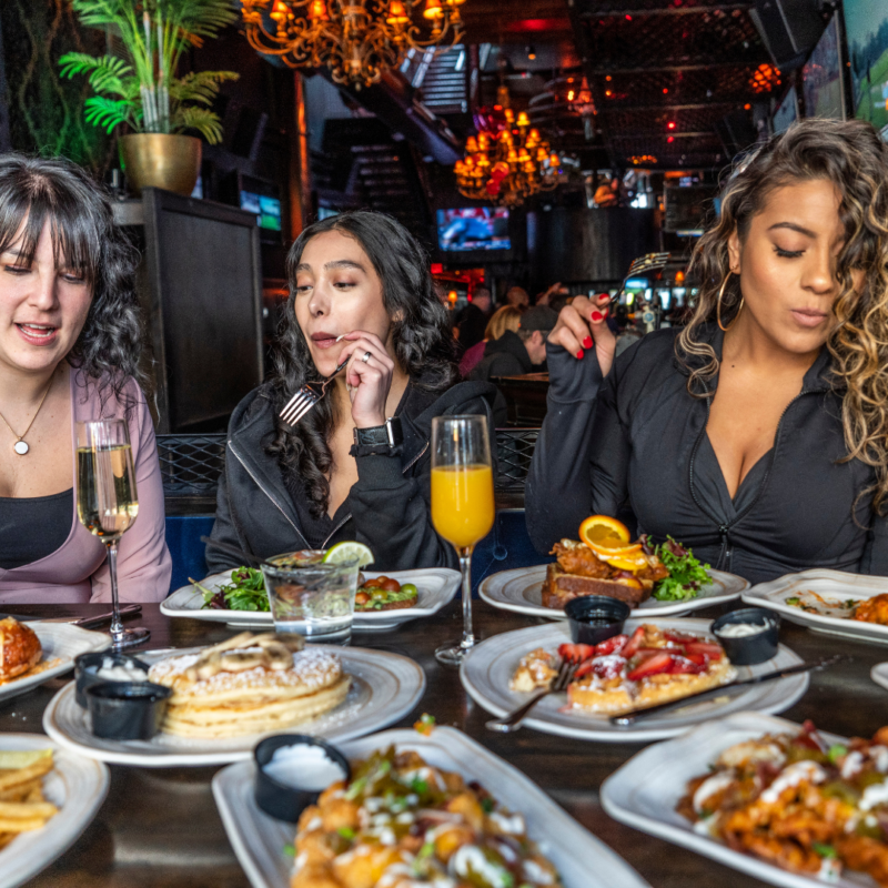 Three women eating brunch at Six26 with a table full of brunch dishes and drinks