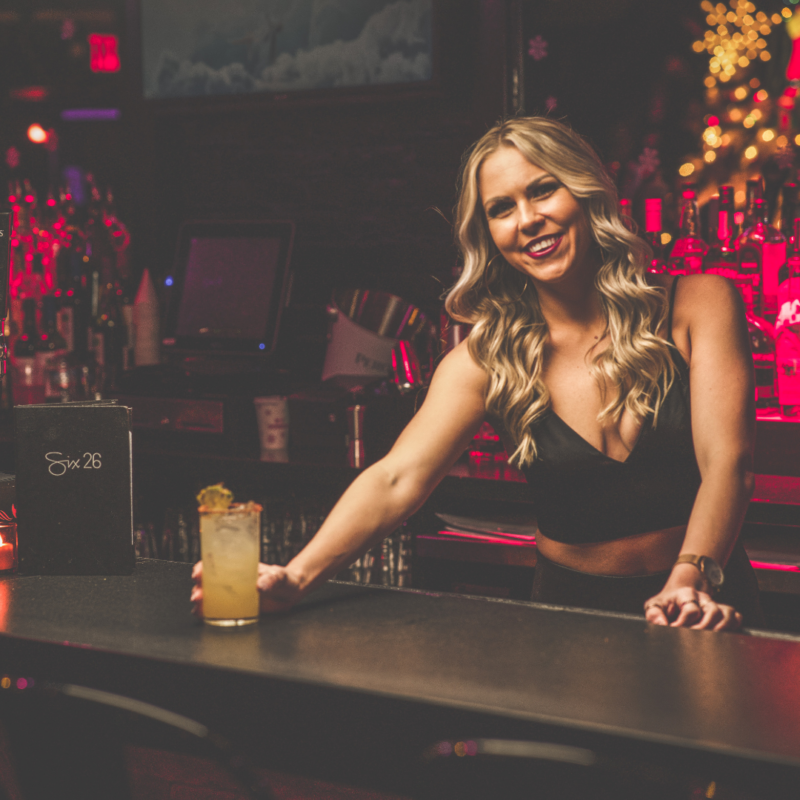 Blonde bartender with cocktail in hand standing behind dimly lit bar