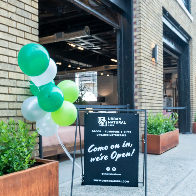 Green and white balloons next to a sign that says "come on in we're open" outside the Urban Natural showroom. 