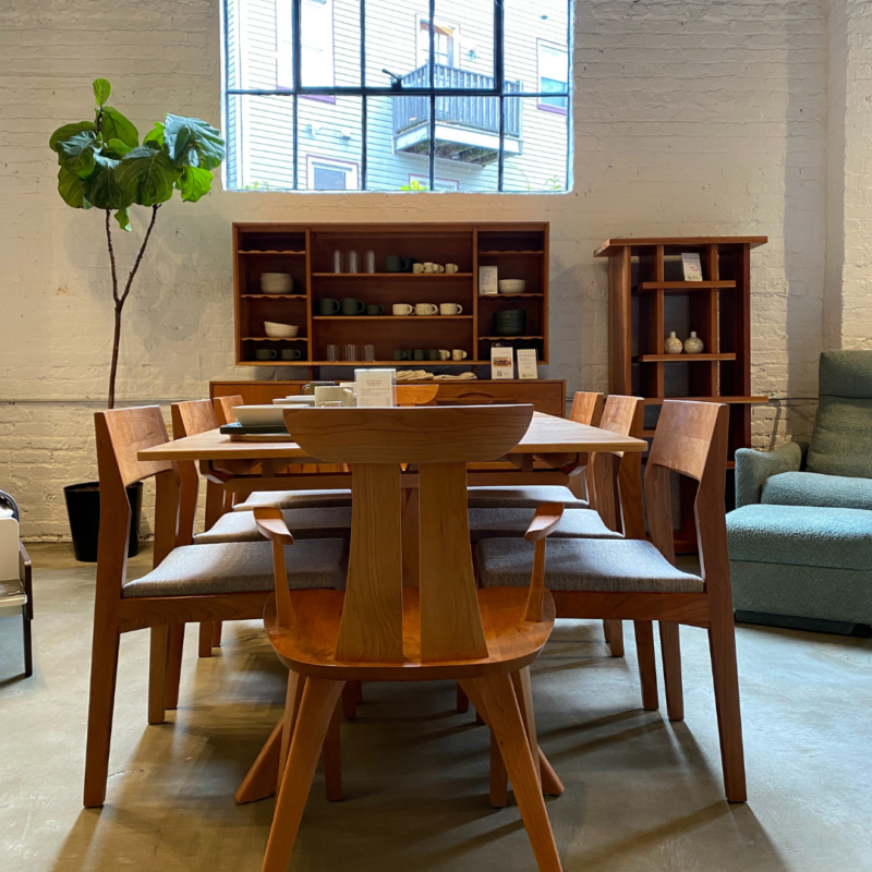 Dining room table with chairs in Urban Natural showroom. A large plant and window are in the background.