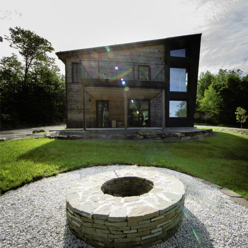 Exterior view of a multi-story Catskill Project home with a fire pit and large grassy yard in the foreground of the image