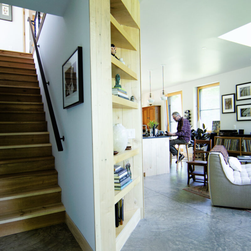 Downstairs in one of the Catskill Project homes with a view of a staircase and the kitchen with a man sitting on a barstool at the island