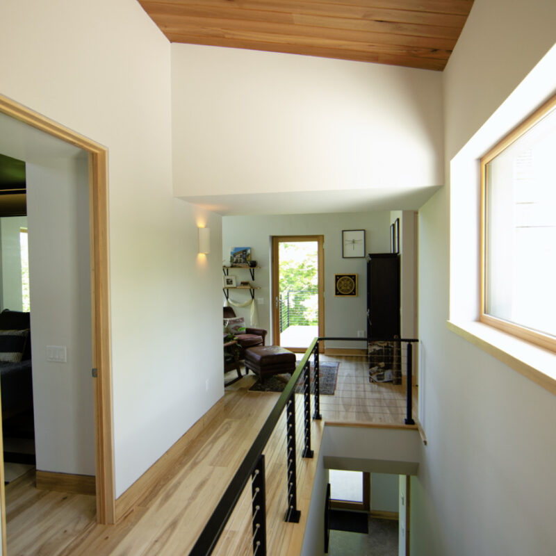 Hallway view in a Catskill Project home with large windows, white walls, wood accents, and natural light
