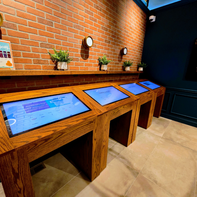 Four digital display screens in front of exposed brick wall at Emerald Tea Supply Co