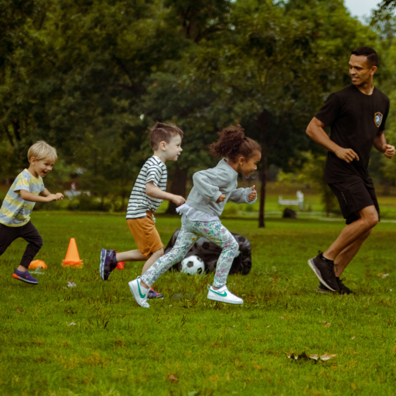 Three kids and a coach running on the soccer field