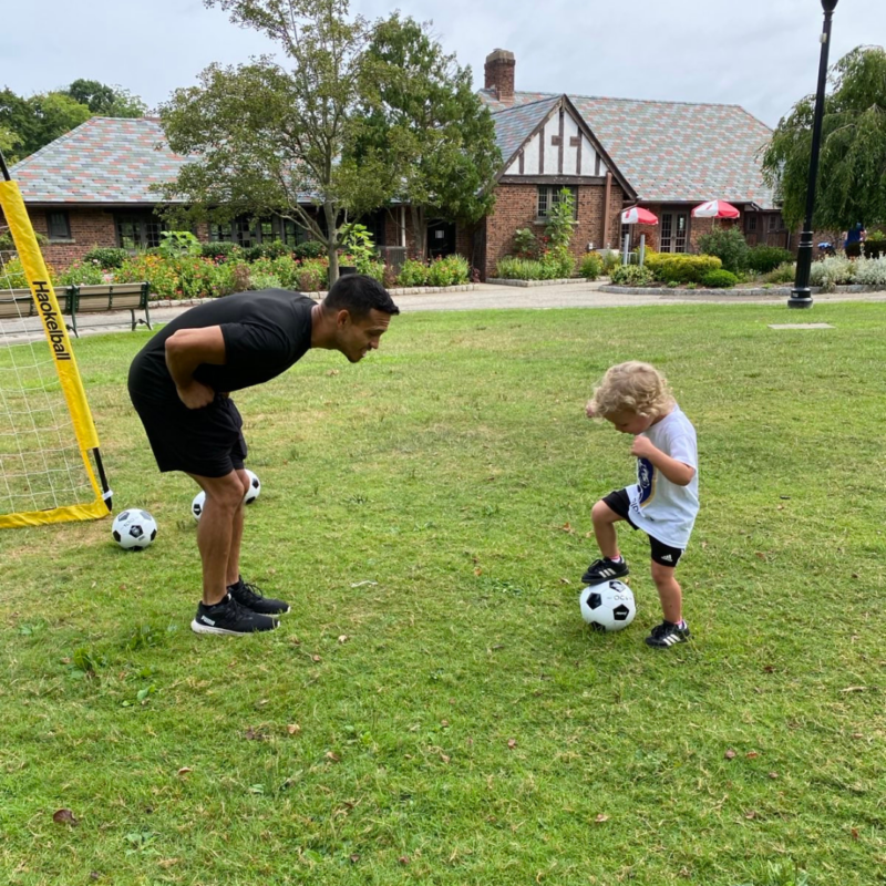 A coach bending over to speak to a young kid with a soccer ball