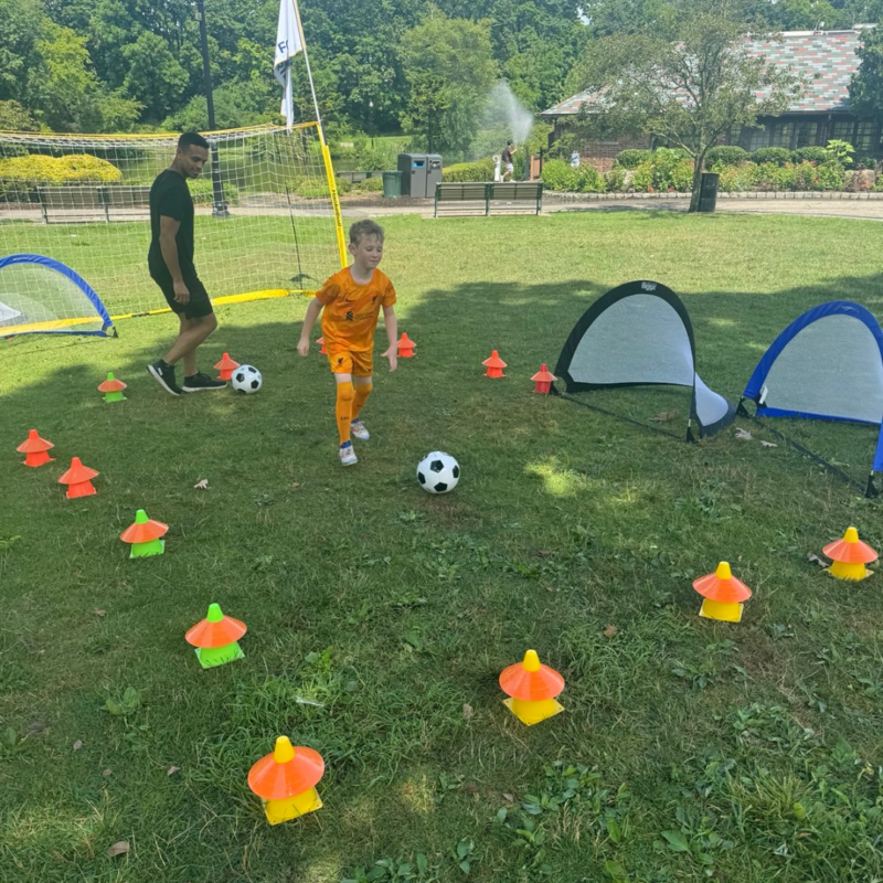 Coach and a kid with soccer balls surrounded by yellow, green, and orange cones practicing on a field