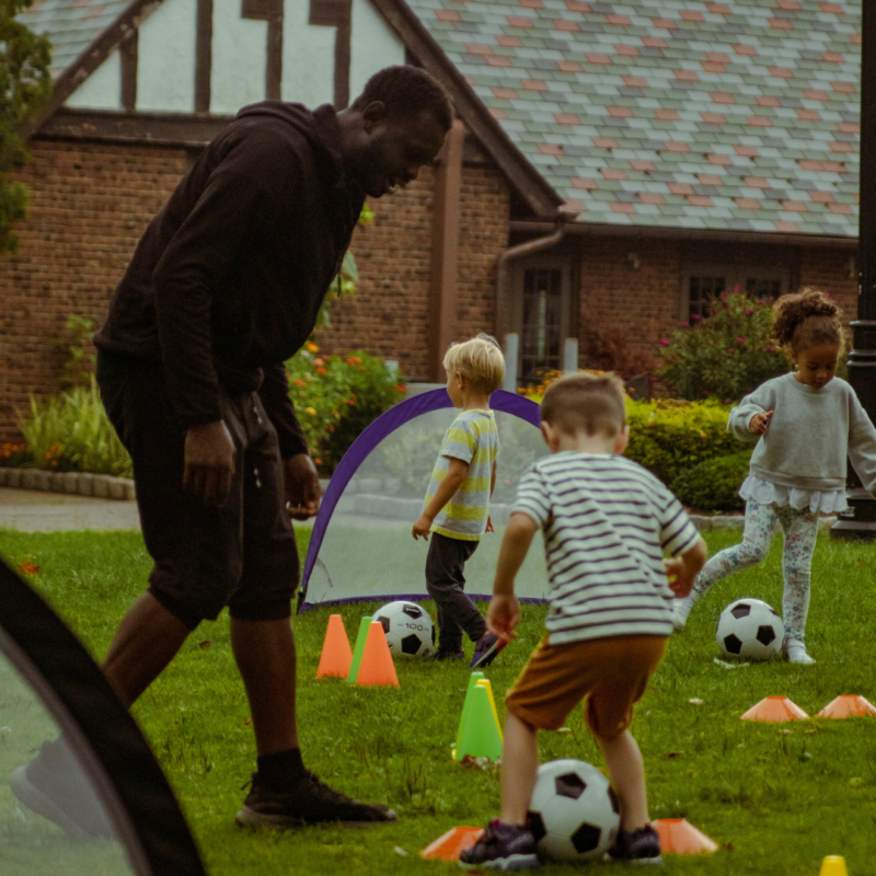 Three kids and a coach with a small soccer coal and three soccer balls