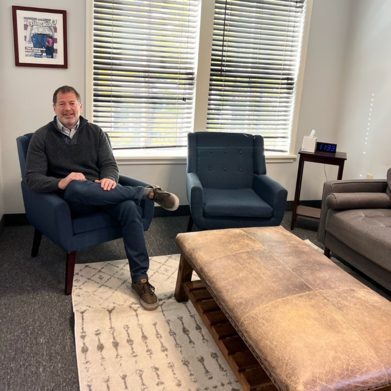 Dr. Ron Wasser sitting in a blue chair with an empty chair beside him