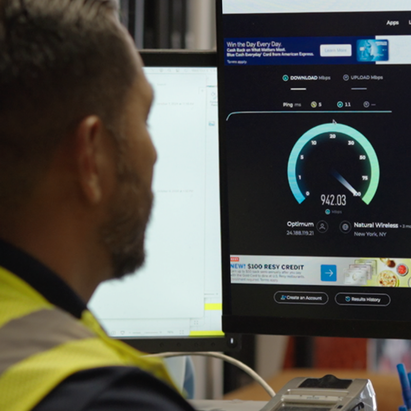 Man wearing a yellow vest looking at internet speeds on a computer