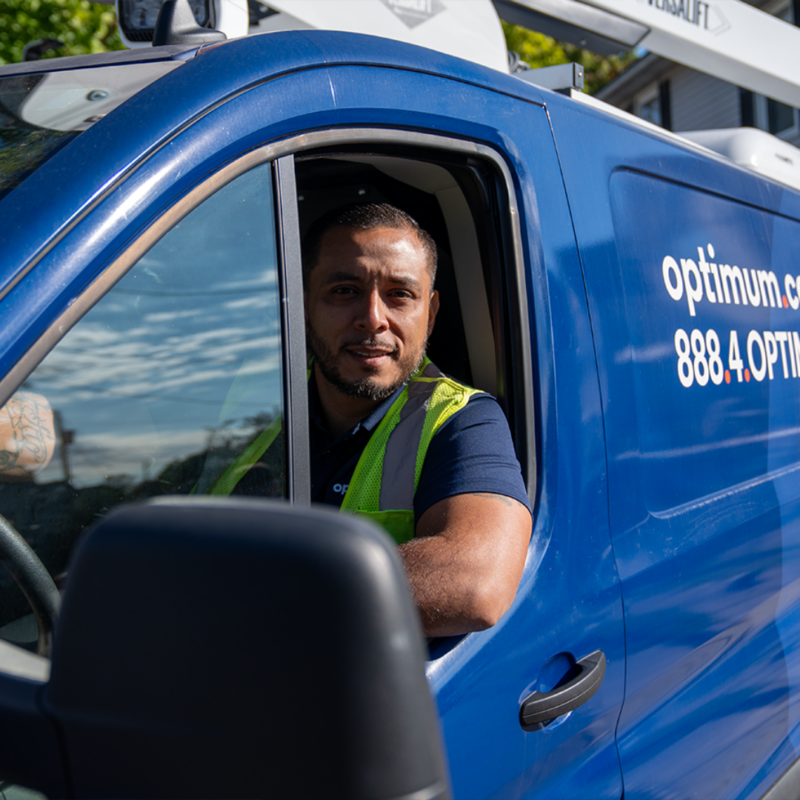 Man in a yellow vest driving a blue Optimum van